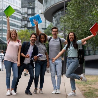 Excited group of students celebrating an accomplishment with arms up and looking at the camera smiling â education concepts